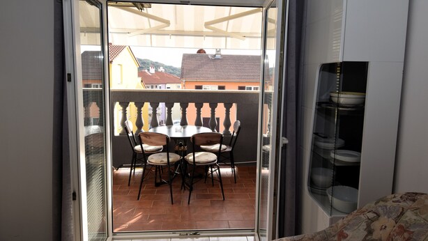 Varanda com mesa e cadeiras de jantar, porta de vidro e prateleira com louças.