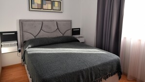 Quarto bem arrumado com cabeceira estofada cinza, colcha com padrão cinza, mesas de cabeceira com abajures pretos e uma obra de arte abstrata emoldurada na parede.