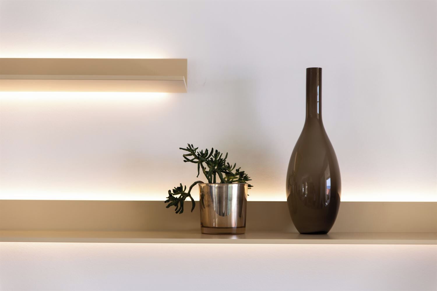 Una estantería minimalista con un florero metálico y una planta en una maceta reflectante.