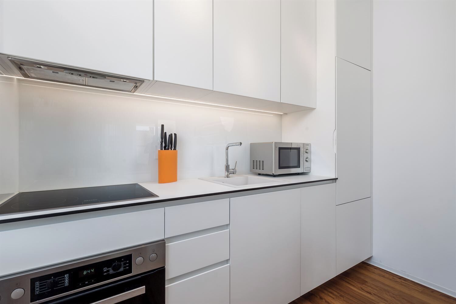 Una cocina moderna con armarios blancos, una campana extractora de acero inoxidable, un microondas y un lavamanos.
