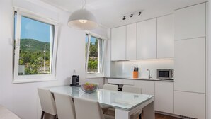 Eine moderne Küche mit weißen Schränken, einem Glastisch und Blick auf Grünflächen.