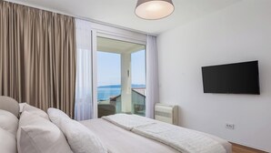 Ein Schlafzimmer mit einem Bett, einem Fernseher, einem Fenster mit Vorhängen und Meerblick.