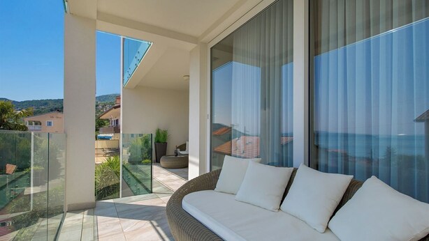 Ein Balkon mit einer Couch, Glastrennwand und Blick auf das Meer und Gebäude.