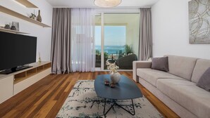 Ein modernes Wohnzimmer mit Flachbildfernseher, einer Couch, einem Couchtisch und Meerblick durch große Fenster.
