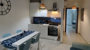 Uma cozinha moderna com vista para o mar, armários brancos, forno embutido e luminárias pendentes.