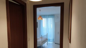 Um corredor leva a um quarto com uma cama, um lustre pendurado e uma porta à esquerda.