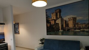 Sala de estar com uma grande pintura de um castelo, um sofá azul e uma área de jantar com mesa e cadeiras.