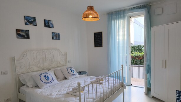 Quarto bem arrumado com cama, luminária pendente e vista para o exterior através de uma porta.