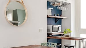 A dining area with a wooden table and green chairs, a microwave, and a shelf with kitchenware. - Piermarini Suite in the historical center of Monza- 15 min from Milan (Monza)