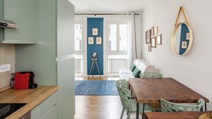 A modern kitchen with a red coffee machine, a dining area with a wooden table and green chairs, and a blue accent wall. - Piermarini Suite in the historical center of Monza- 15 min from Milan (Monza)