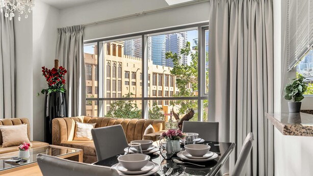 Una sala de estar moderna con una mesa de comedor de cristal, sofás color beige y un ventanal con vistas a la ciudad.