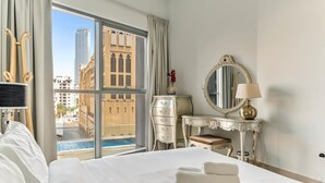 Habitación de hotel con una cama grande, un aparador, un tocador con espejo y vistas a un edificio y una piscina a través de la ventana.