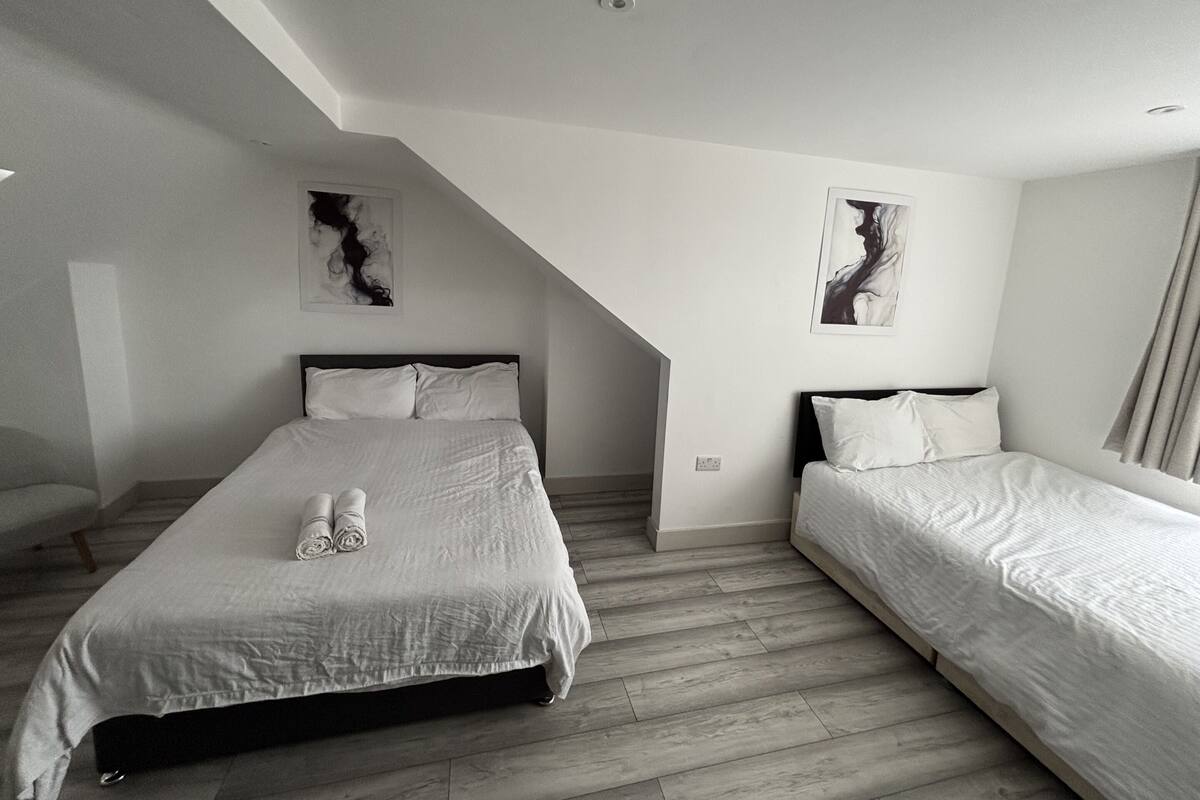 A modern bedroom with two beds, a sloped ceiling, and abstract wall art.