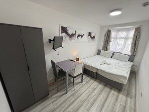Una habitación de hotel pequeña con cama, escritorio con silla, armario y cuadros en la pared.