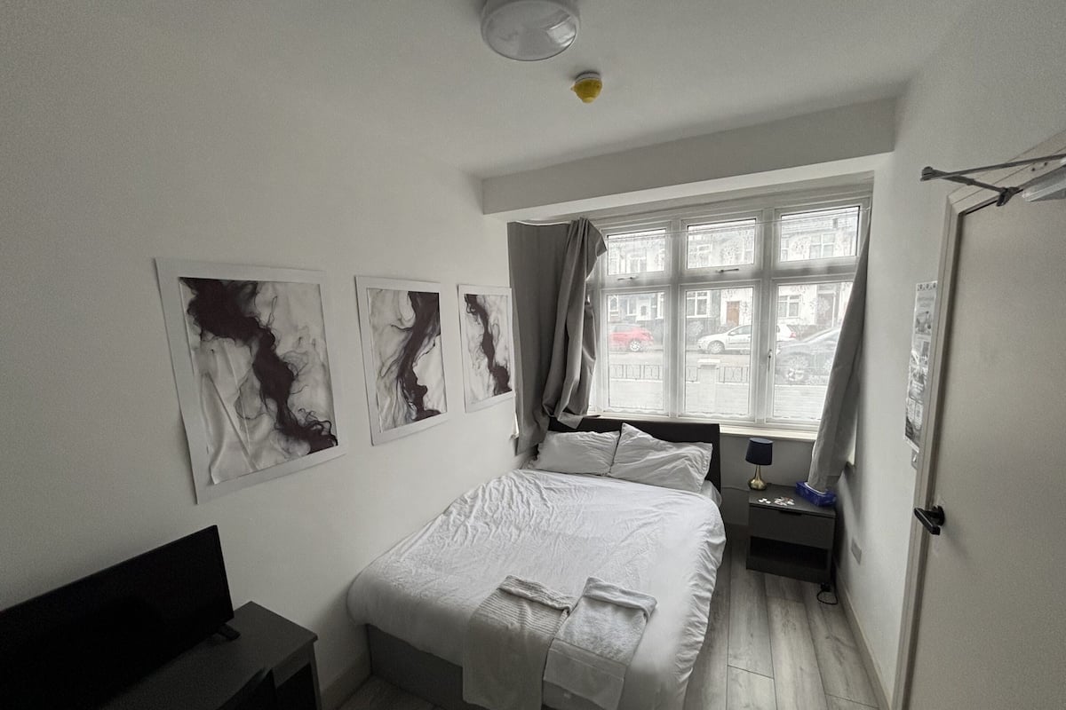 A bedroom with a bed, a desk, and a window with a view of the street.