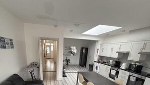 Cozinha moderna com armários brancos, sala de jantar com mesa e cadeiras, e corredor que leva a outro cômodo.