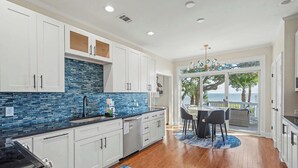 A modern kitchen with white cabinets, a blue-tiled backsplash, and a dining area with a view of the ocean. - 10 River Club (Fripp Island)