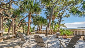 A wooden deck with Adirondack chairs, surrounded by palm trees and overlooking a body of water. - 10 River Club (Fripp Island)