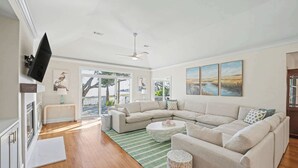 A spacious living room with a large sectional sofa, a flat-screen TV mounted on the wall, and a ceiling fan. - 10 River Club (Fripp Island)