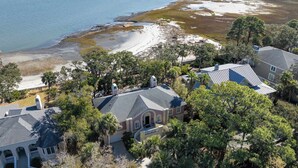 A coastal property with a beach, a large house with a grey roof, and surrounding trees. - 10 River Club (Fripp Island)