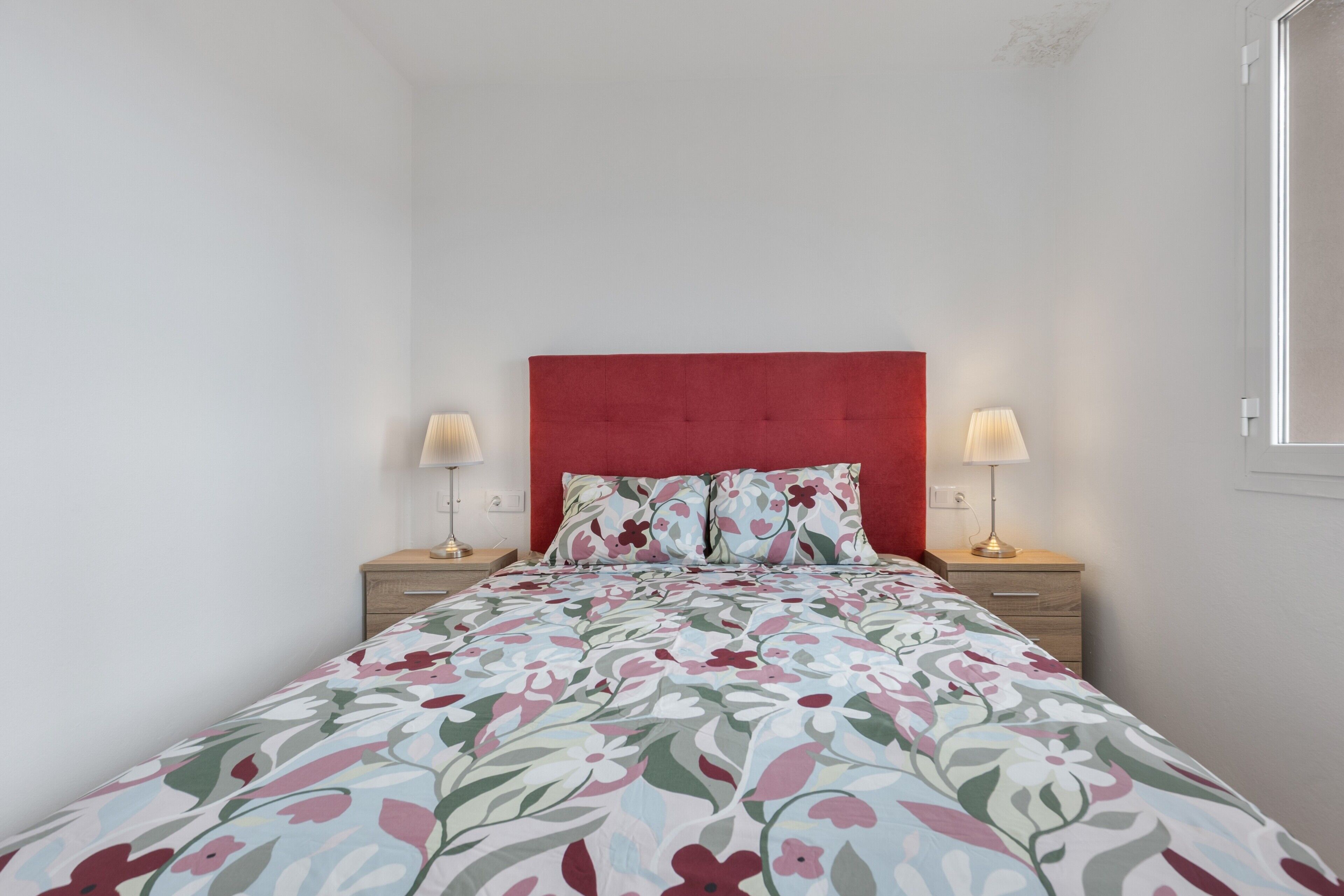 Une chambre à coucher avec une tête de lit rouge, une literie à motifs floraux, deux lampes de chevet et une table de chevet.