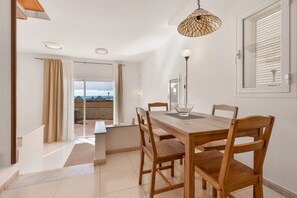 Een eetruimte met een houten tafel en stoelen, een hanglamp en uitzicht door een glazen deur.