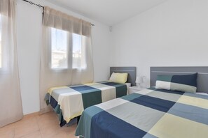 Een kamer met twee bedden, een raam met gordijnen, een nachtkastje met een lamp en een lichtschakelaar aan de muur.