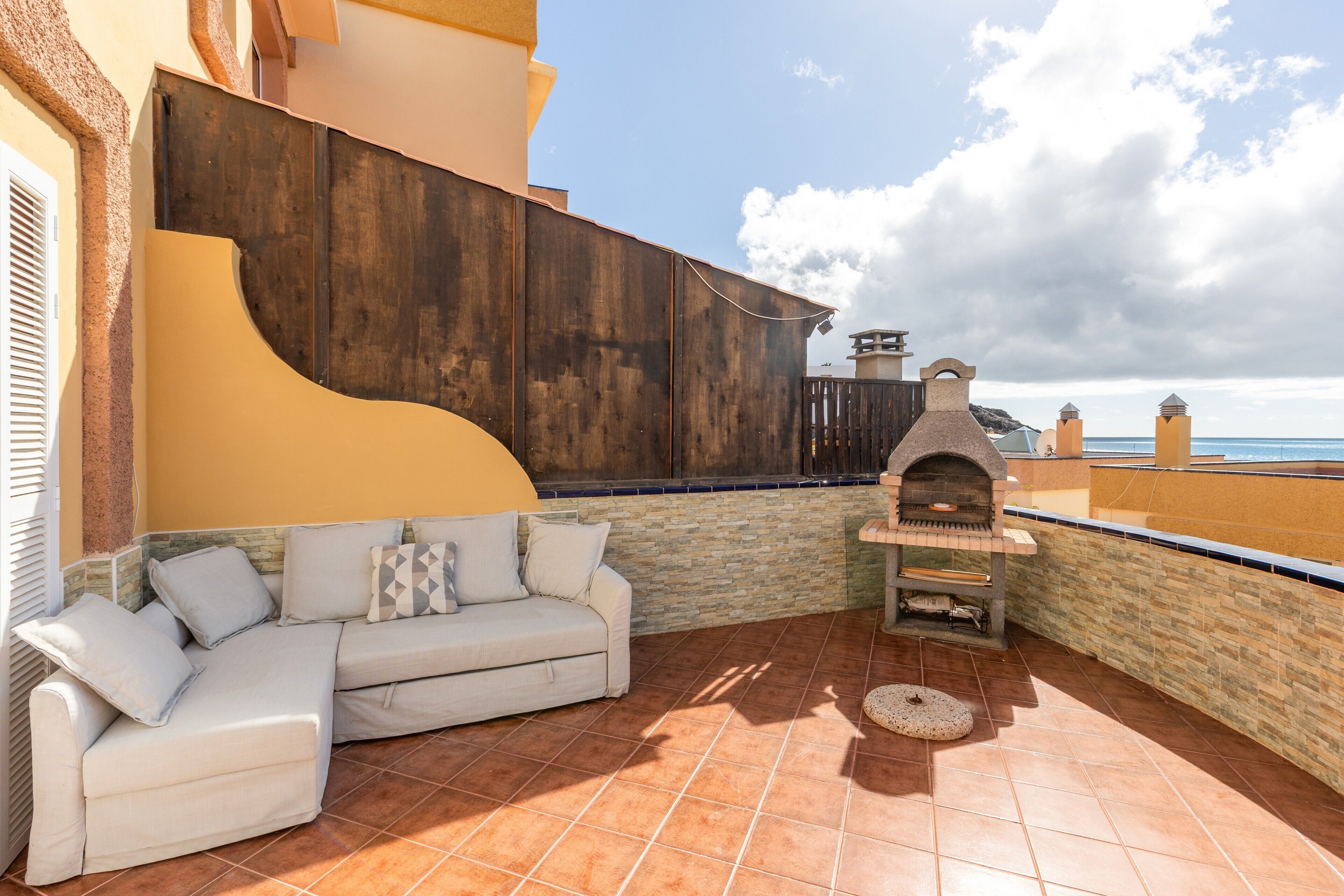 Eine Terrasse mit einer weißen Couch, einer Steinwand und einem Backofen aus Ziegeln.