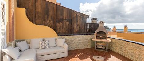 Eine Terrasse mit einer weißen Couch, einer Steinwand und einem Backofen aus Ziegeln.