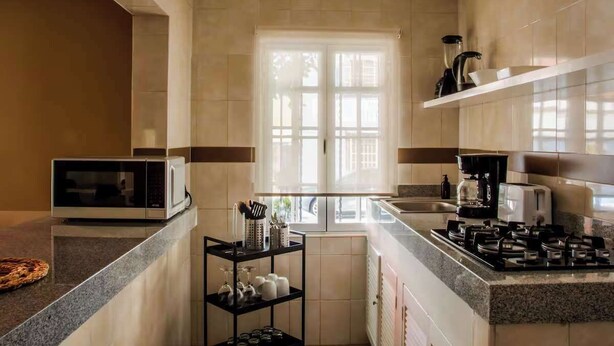 Eine moderne Küche mit Mikrowelle, Herd und Kaffeemaschine. Ein Fenster sorgt für natürliches Licht, und ein Regal bietet Platz für Küchenutensilien.