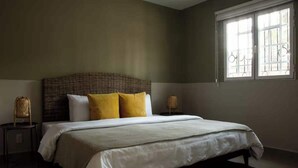 Ein Schlafzimmer mit einem großen Bett, zwei Nachttischen und einem Fenster mit Gitterstäben.
