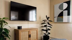Ein modernes Wohnzimmer mit einem an der Wand montierten Flachbildfernseher, einem Holzschrank mit Flechtfront, einer Topfpflanze und einem modernen abstrakten Gemälde.