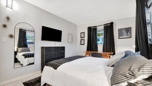 A modern bedroom with a large bed, a flat-screen TV, a dresser, and a window with curtains. - Family Home 10 Mins to Beach Pets Welcome (Gulfport)