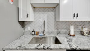 A kitchen with white cabinets, a stainless steel sink, a herringbone tile backsplash, and a fire extinguisher mounted on the wall. - Family Home 10 Mins to Beach Pets Welcome (Gulfport)