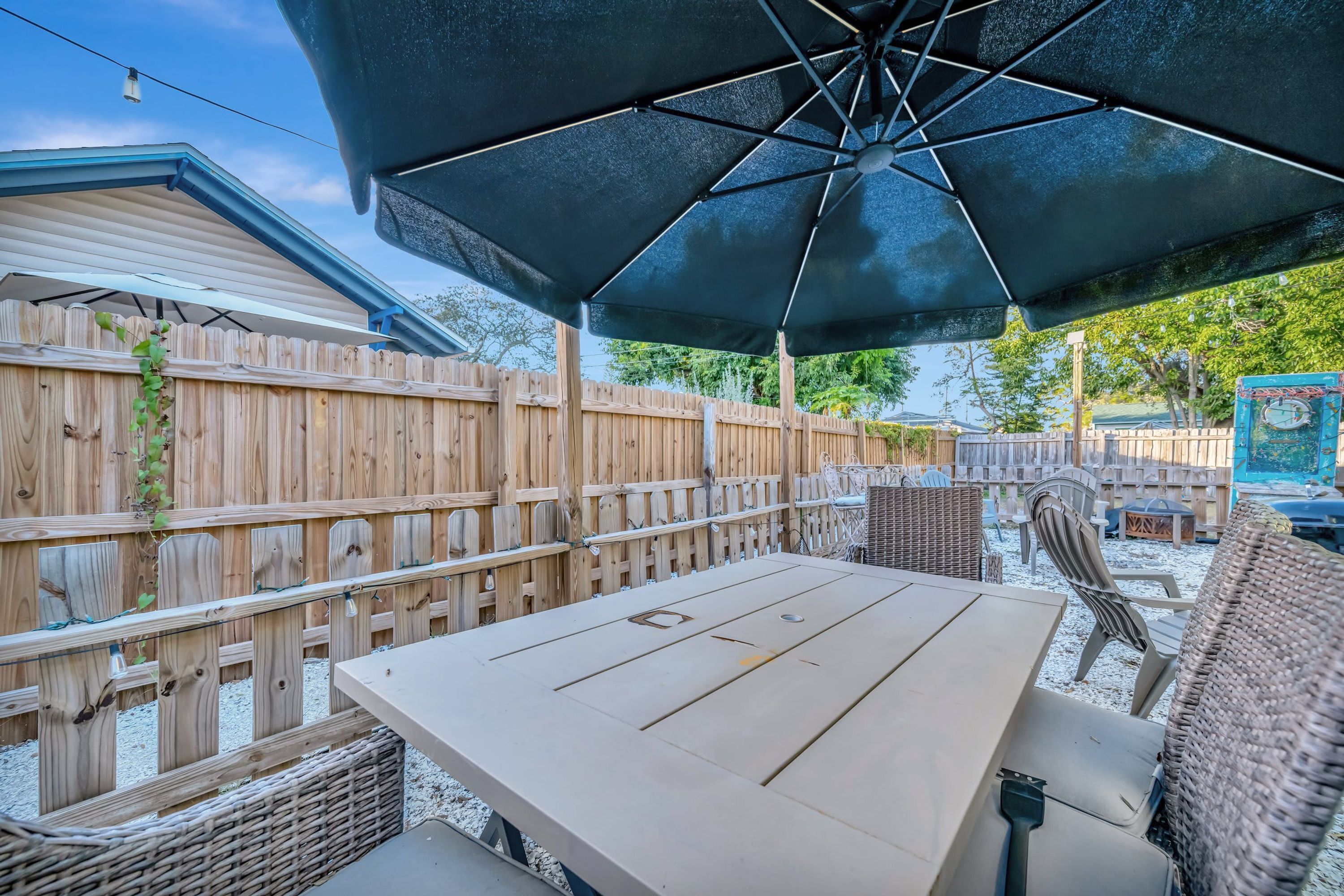 An outdoor patio with a table and chairs, a large umbrella, and a wooden fence.