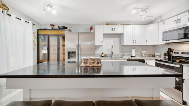A modern kitchen with white cabinets, a black countertop, and stainless steel appliances. - Family Home 10 Mins to Beach Pets Welcome (Gulfport)