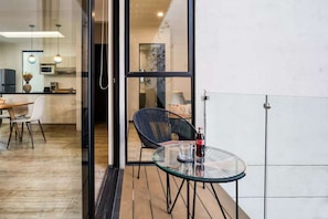 Eine moderne Küche mit Edelstahlgeräten, ein Essbereich mit Glastisch und Stühlen sowie ein Blick durch eine Glastür in einen Wohnraum mit Sofa und Lampe.