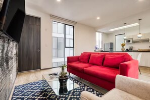 A modern living room with a red sofa, a glass coffee table, and a patterned rug. - HOM Roma l Unique 1 BR in Mexico City (Mexico City)