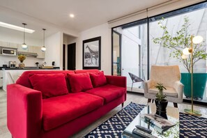 Ein modernes Wohnzimmer mit einem roten Sofa, einem Glastisch und Blick auf die Küche und den Balkon.