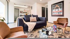A modern living room with a dark sofa, a brown armchair, and a glass coffee table. - HOM Roma Double l Spacious 2 Bedroom in Mexico City (Mexico City)