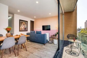 A modern living room with a sofa, dining table, and chairs, a TV mounted on the wall, and a balcony with a table and chairs. - HOM Roma Double l Spacious 2 Bedroom in Mexico City (Mexico City)