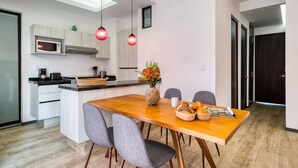 A modern kitchen with white cabinets, a microwave, and a wooden island with seating. There are red pendant lights, a vase with flowers, and a basket of bread on the island. - HOM Roma Double l Spacious 2 Bedroom in Mexico City (Mexico City)