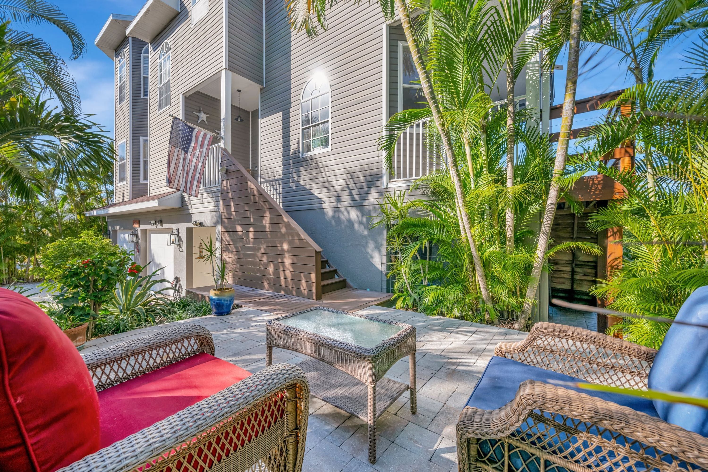 A two-story house with a staircase, outdoor furniture, and tropical plants.