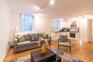 Uma sala de estar moderna com um sofá, uma mesa de centro e uma cadeira. Há uma área de cozinha com armários e eletrodomésticos.