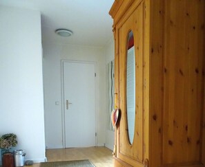 Une pièce avec une armoire en bois, une porte blanche, un petit tapis et une plante en pot.