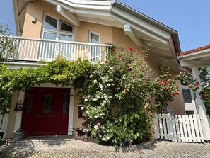 A two-story building with a red door, a balcony with white railings, and a white picket fence. - Apartment 'Findus' with Private Terrace and Wi-Fi (Kempten-Haldenwang)
