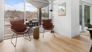 A modern interior with a dining area, two brown chairs, a round table, and a view of a mountainous landscape through large windows. - 5 Star Holiday Home in Glesborg (Glesborg)