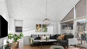 A modern living room with a grey sofa, a round coffee table, and a large window offering a view of the outdoors. - 5 Star Holiday Home in Glesborg (Glesborg)