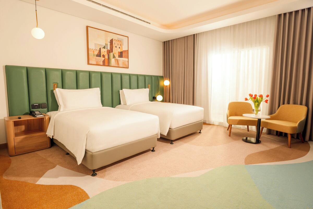 A hotel room with two beds, a nightstand, a chair, a small table with a vase, and a painting on the wall.