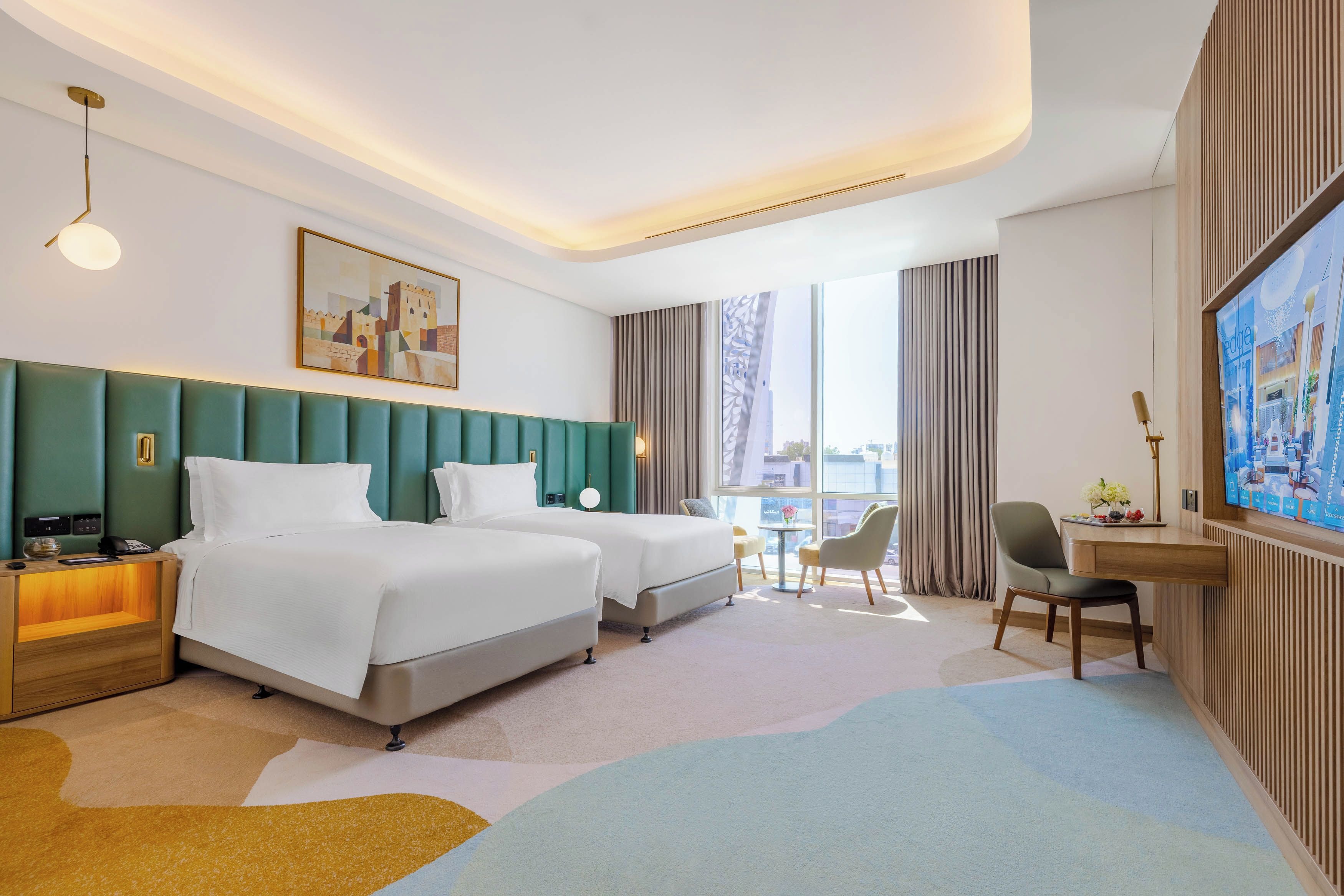 A hotel room with two beds, a desk, a chair, a TV, and a large window.